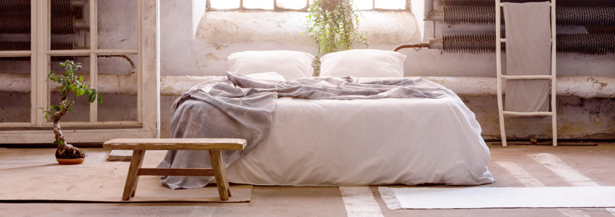 Pillows and blanket on bed in japanese bedroom interior with stool and plant at window. Real photo