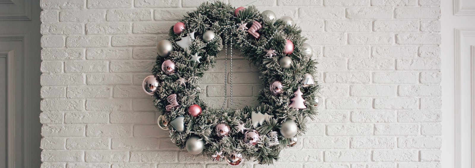 A traditional bright Christmas wreath hanging over the fireplace, on a white brick wall, and packaged gifts are stacked on a fireplace with candles.