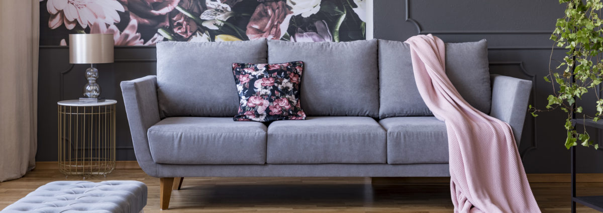Real photo of a living room interior with a sofa, pillow, blanket and flowers on wallpaper