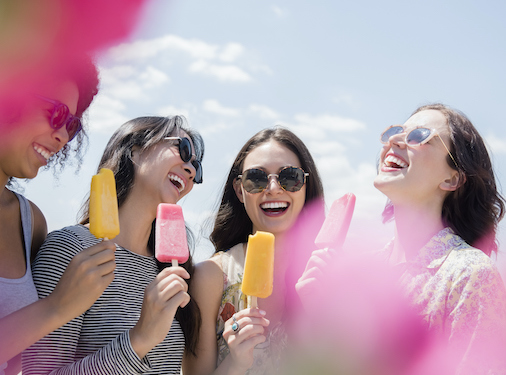 Laughing women eating flavored ice outdoors