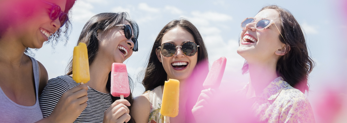 Laughing women eating flavored ice outdoors