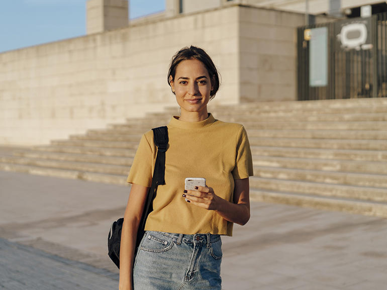 Portrait of smiling young woman holding cell phone outdoors