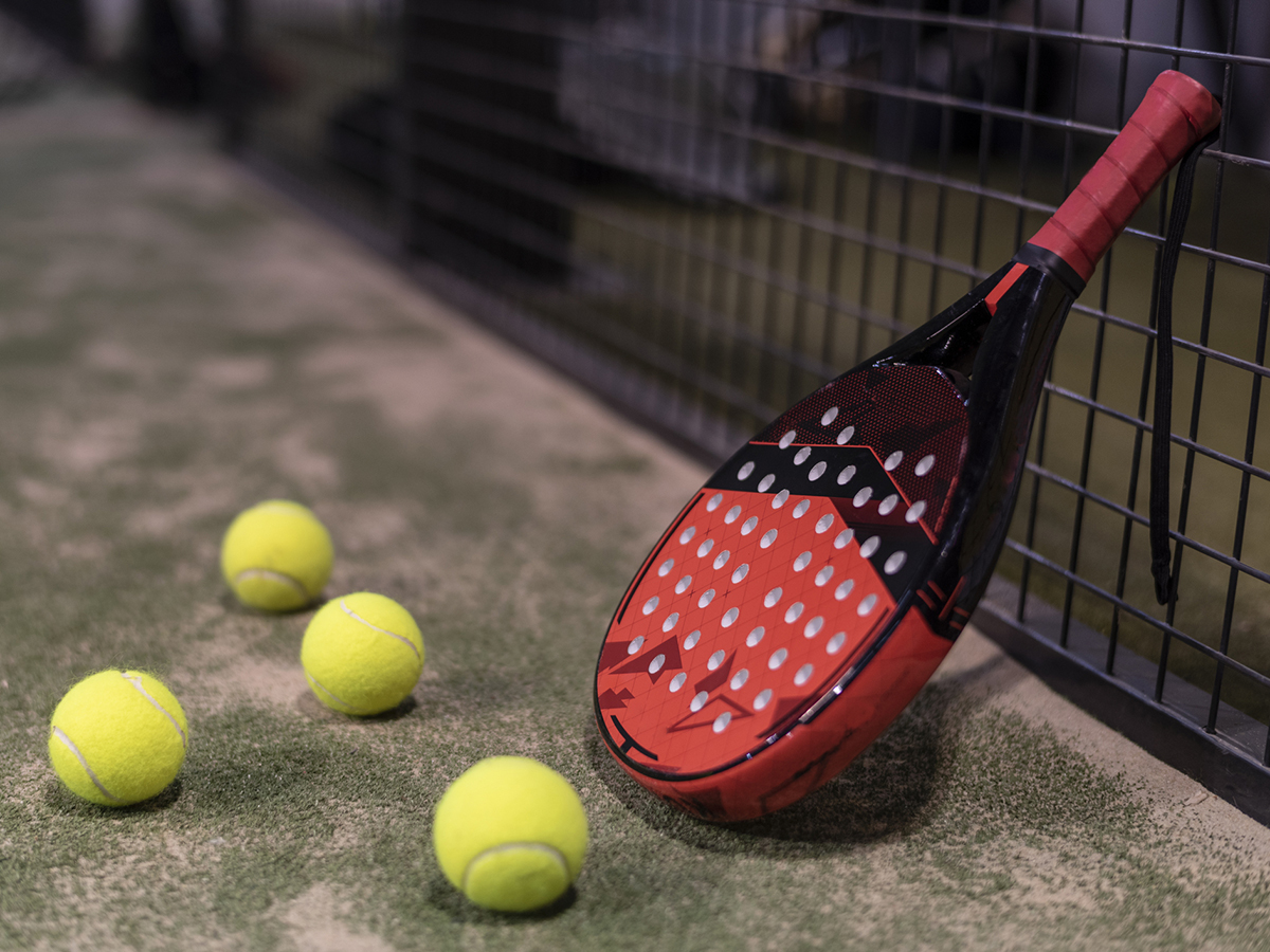 Paddle tennis racket and balls in fence