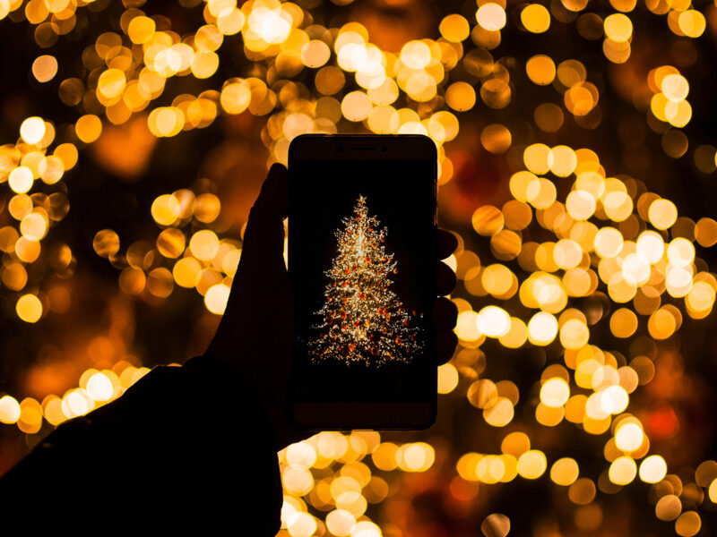 Close-Up Of Person Photographing Illuminated Christmas Tree Using Smart Phone