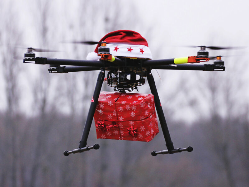 Drone With Santa Hat Carrying Christmas Present Against Sky