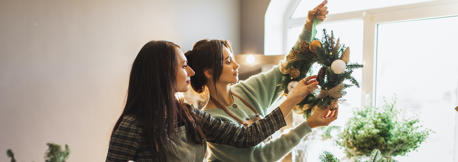 Two women making Christmas wreath using fresh pine branches and festive decorations.