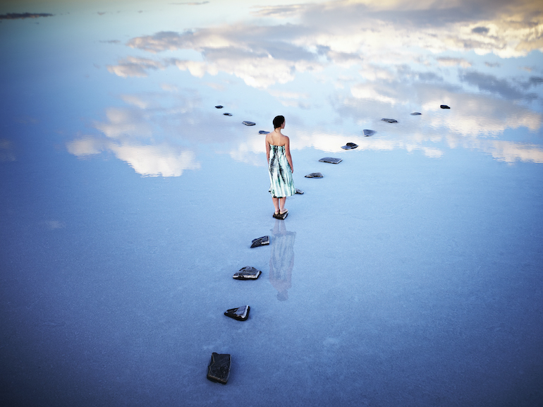 Woman standing at fork in stone pathway in lake