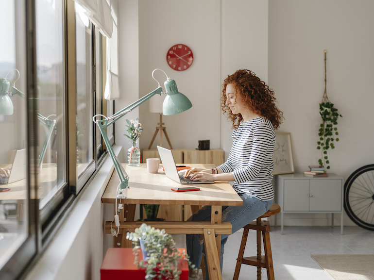 Woman sitting on a desk using a laptop computer while working from home.