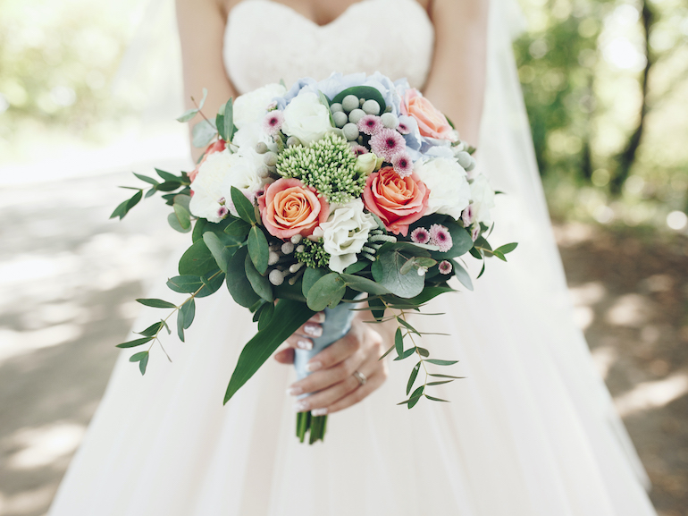 Caucasian bride holding bouquet of flowers outdoors