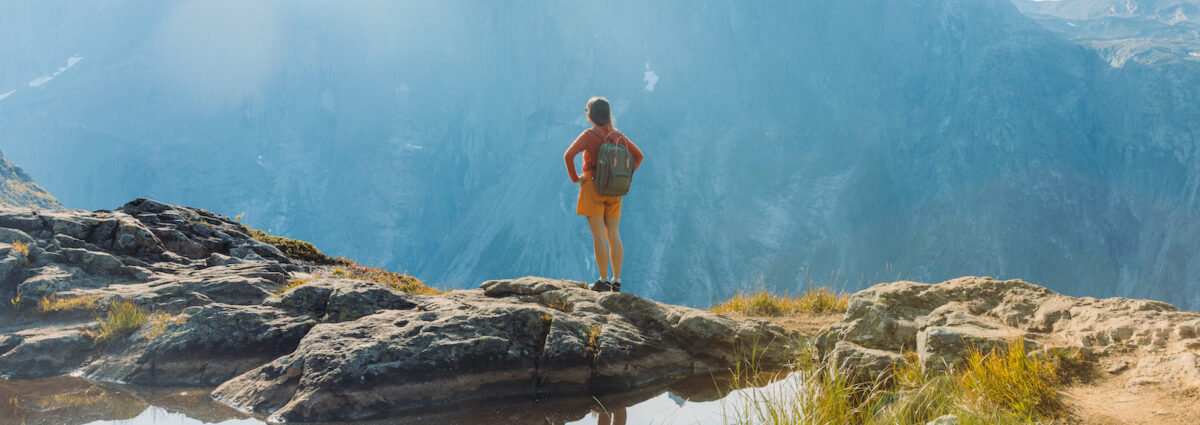 Rear view of a female backpacker hiking in the mountains by the lake in Norway during autumn day
