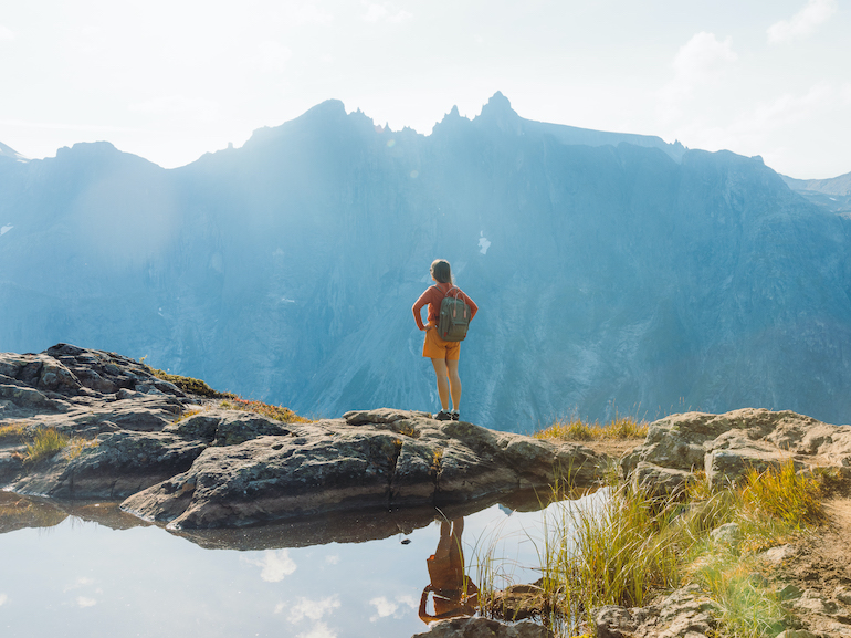 Rear view of a female backpacker hiking in the mountains by the lake in Norway during autumn day