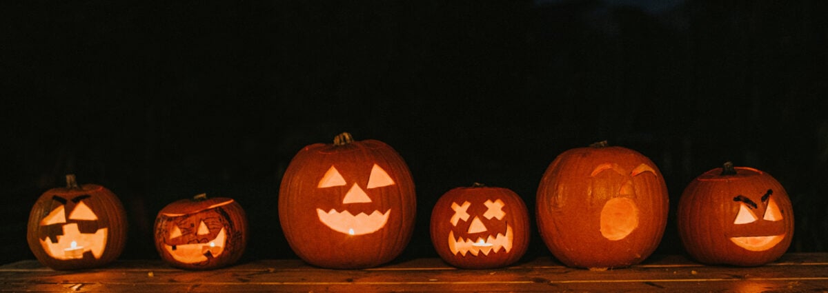 A row of various sized carved Hallowe'en Pumpkins with different facial expressions glowing in the dark. Space for copy.