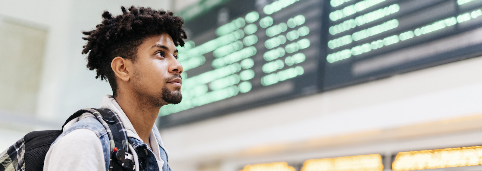 Young man at the airport looking at the list of destinations holding a cell phone.
