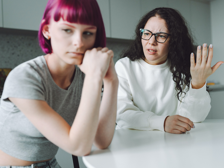 Single working mother and her teenage girl talking sadly in the kitchen