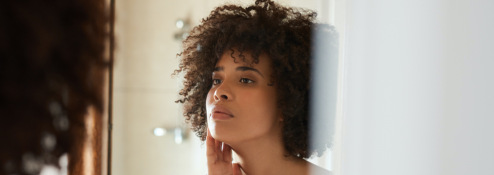 Young African woman examining her skin in a bathroom mirror