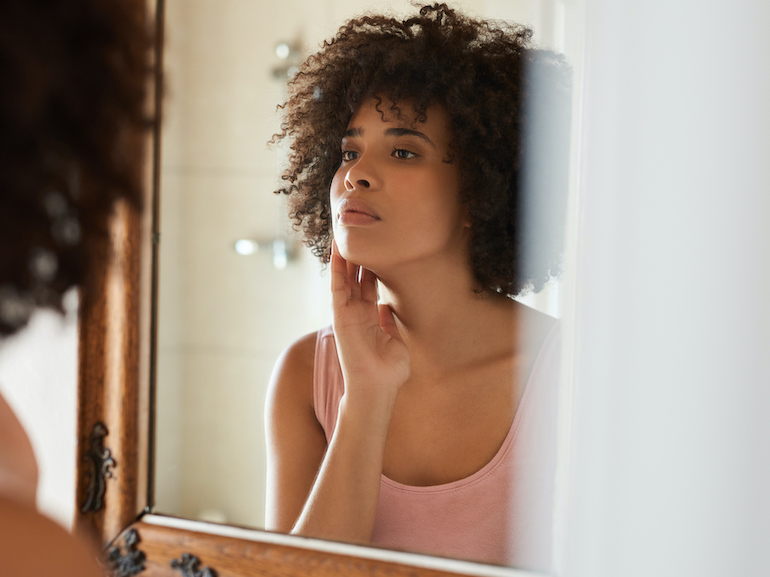 Young African woman examining her skin in a bathroom mirror