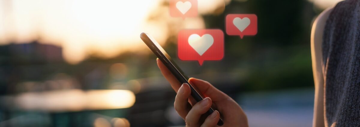 Close up of young woman checking social media network on smartphone on the go in the city. Mobile phone with heart emoji speech bubble message on the screen. People engaging in networking with technology. Social media addiction concept