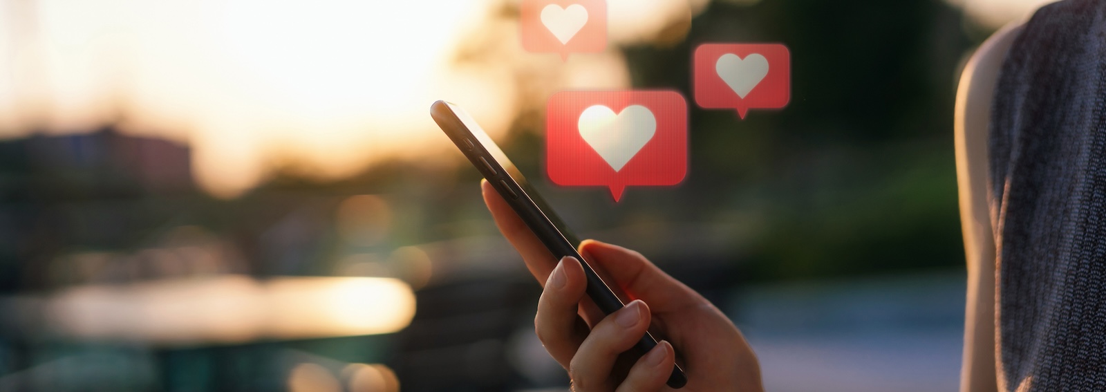 Close up of young woman checking social media network on smartphone on the go in the city. Mobile phone with heart emoji speech bubble message on the screen. People engaging in networking with technology. Social media addiction concept