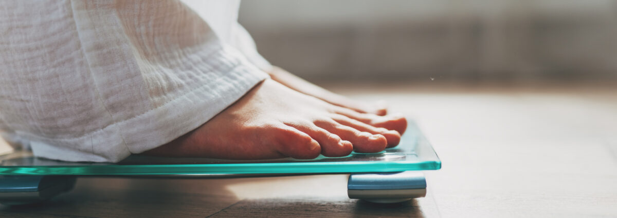 Female feet standing on electronic scales for weight control on wooden background. The concept of slimming and weight loss