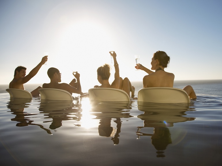 Friends drinking in infinity pool near ocean
