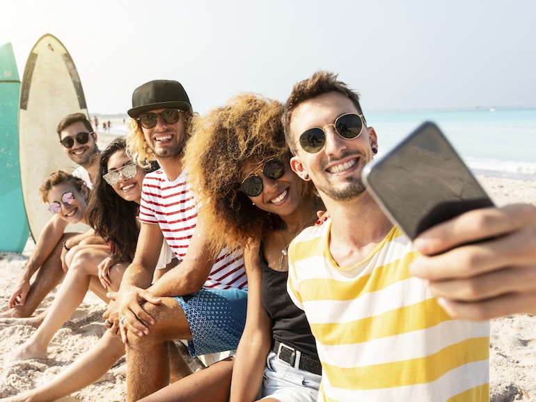 Friends sitting on the beach, having fun, taking selfies