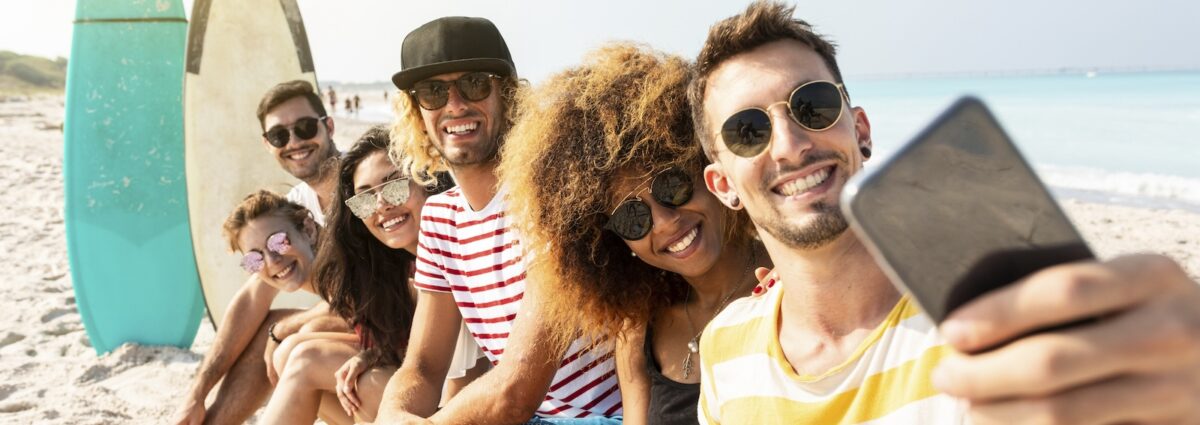 Friends sitting on the beach, having fun, taking selfies