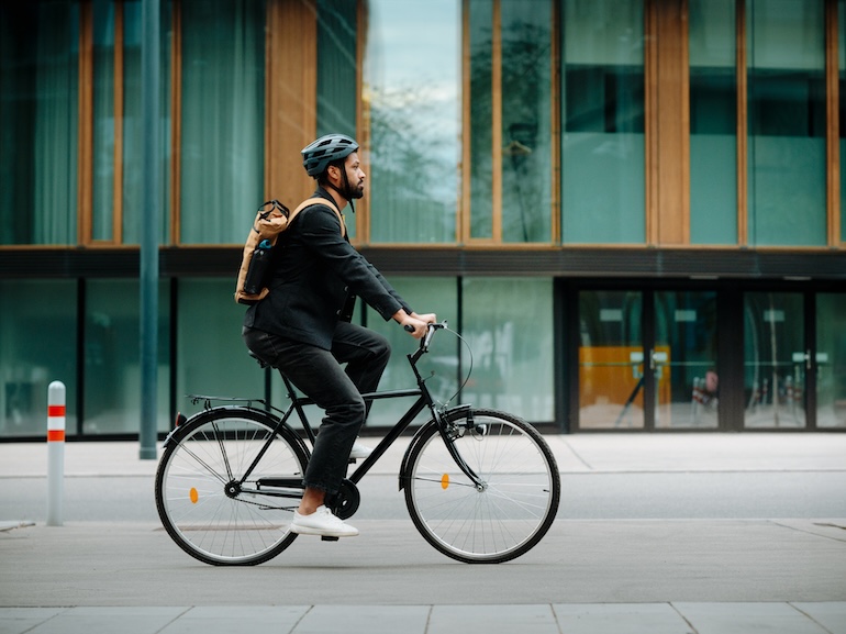 Side view of a city commuter riding to work on a bicycle. Young single businessman traveling from work to home on a bike, wearing a backpack and helmet for safety. City lifestyle of single man.