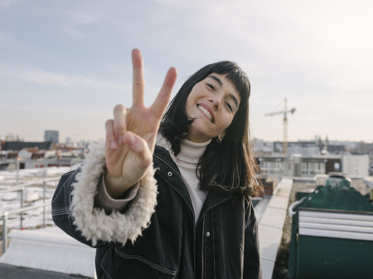 Portrait Of Woman Giving Peace Sign While Standing On Rooftop