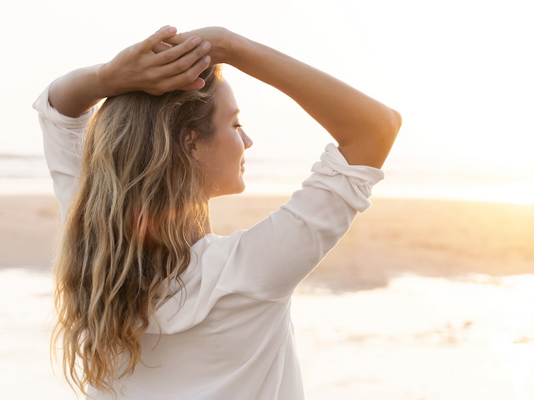 Woman with hands behind head standing at beach