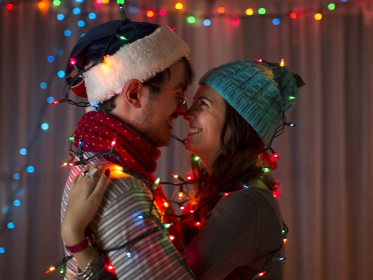 Romantic young couple wrapped in decorative lights at christmas