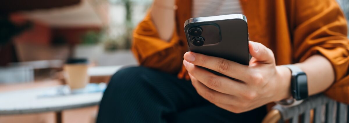 Close up shot of a young Asian woman using smartphone while sitting in an outdoor cafe and drinking coffee. Lifestyle and technology