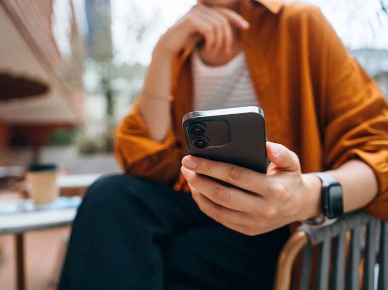 Close up shot of a young Asian woman using smartphone while sitting in an outdoor cafe and drinking coffee. Lifestyle and technology