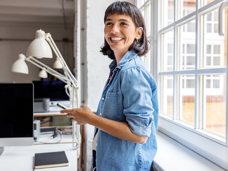 Young businesswoman standing by the window with mobile phone at startup office