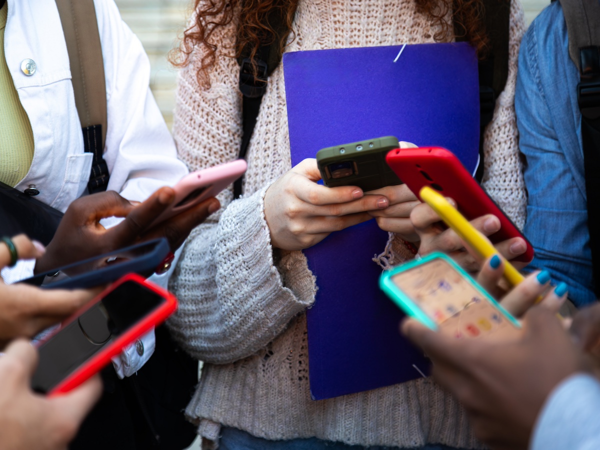 Close up of young college students hands holding mobile phones. Teenagers addicted to smartphones and technology. Group of friends sharing content on social media.