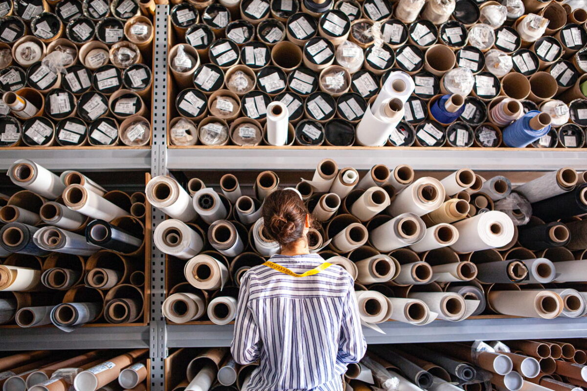 Portrait of textile designer choosing fabric from stack of rolls inside sustainable workshop
