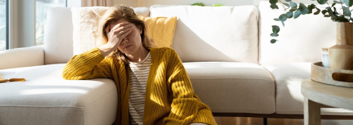 Woman having headache and holding her head while sitting on the floor at home