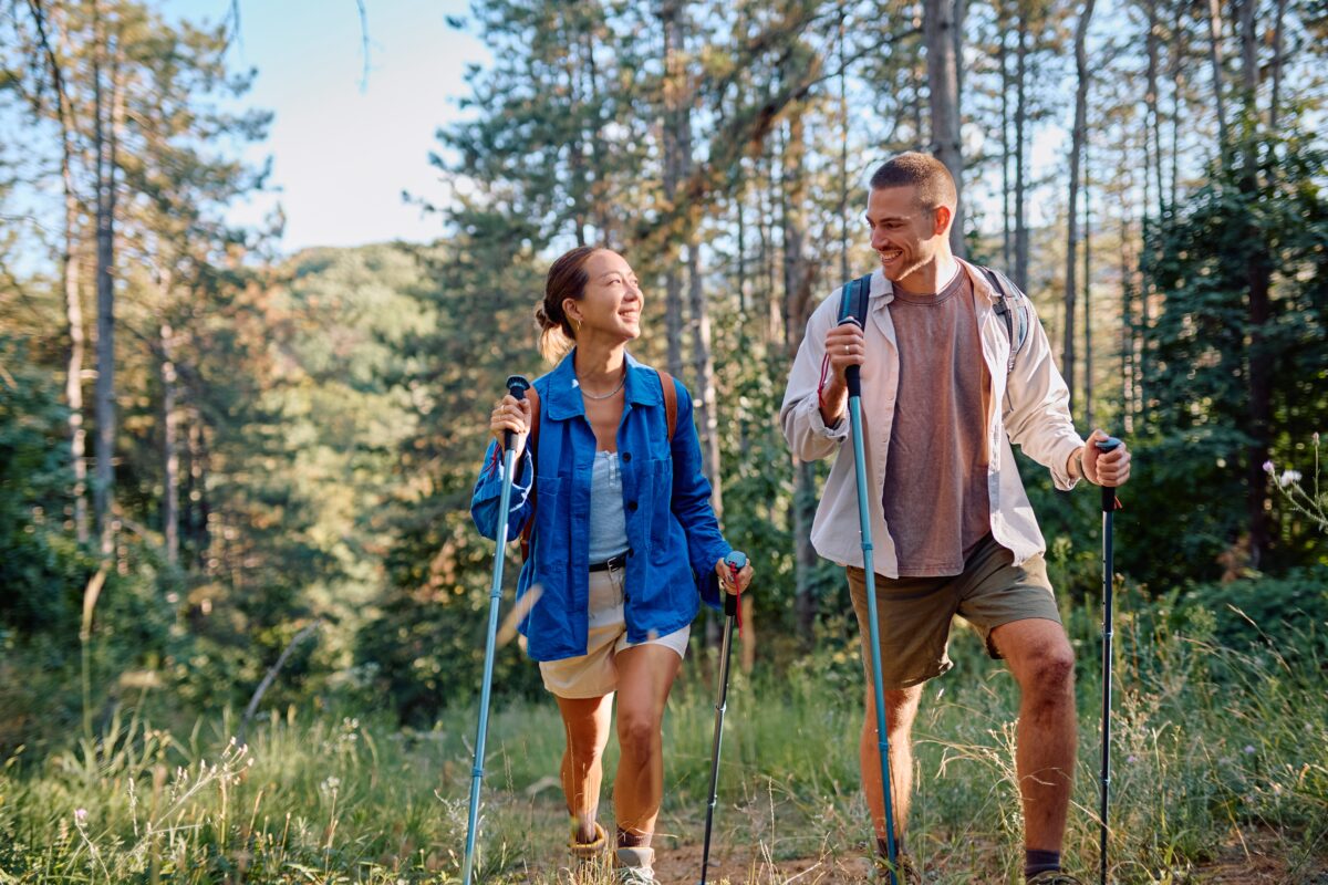 Couple,Walking,Through,A,Lush,Forest,,Using,Trekking,Poles,,Enjoying